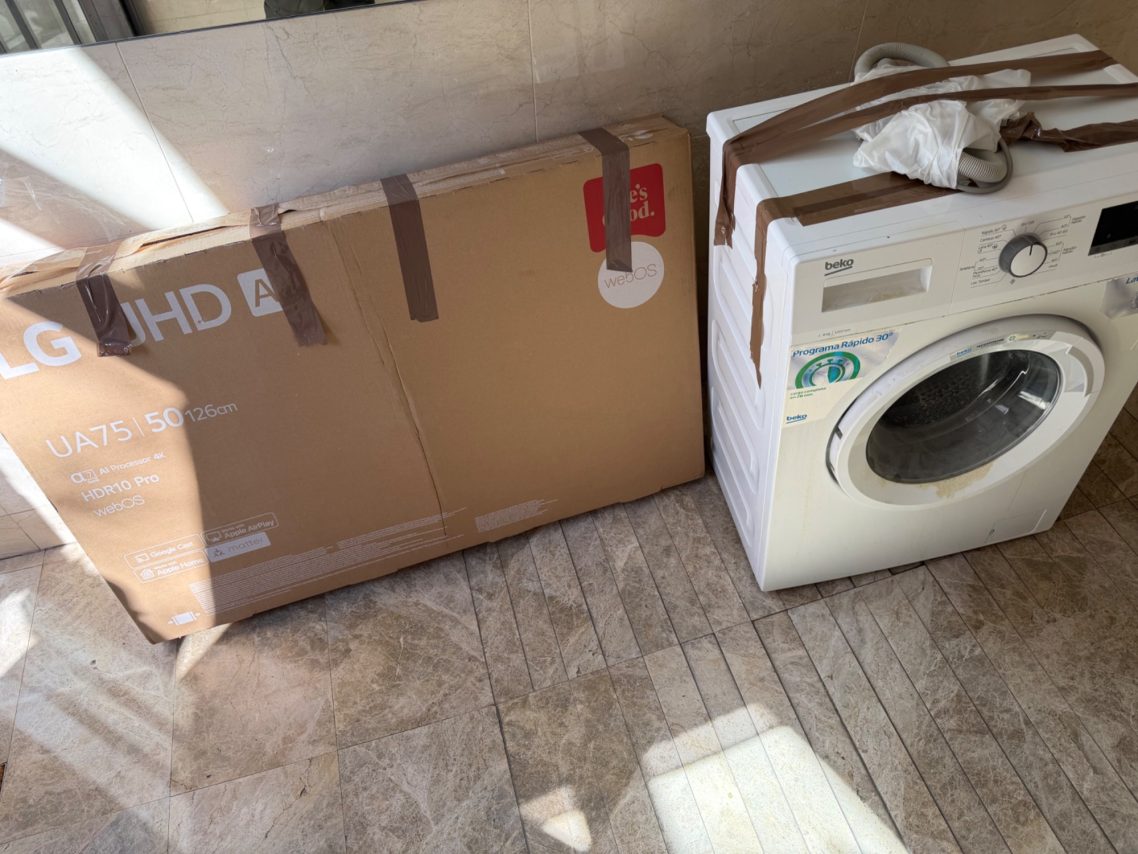 Lavadora blanca al lado de una caja grande, colocada en un ambiente interior.